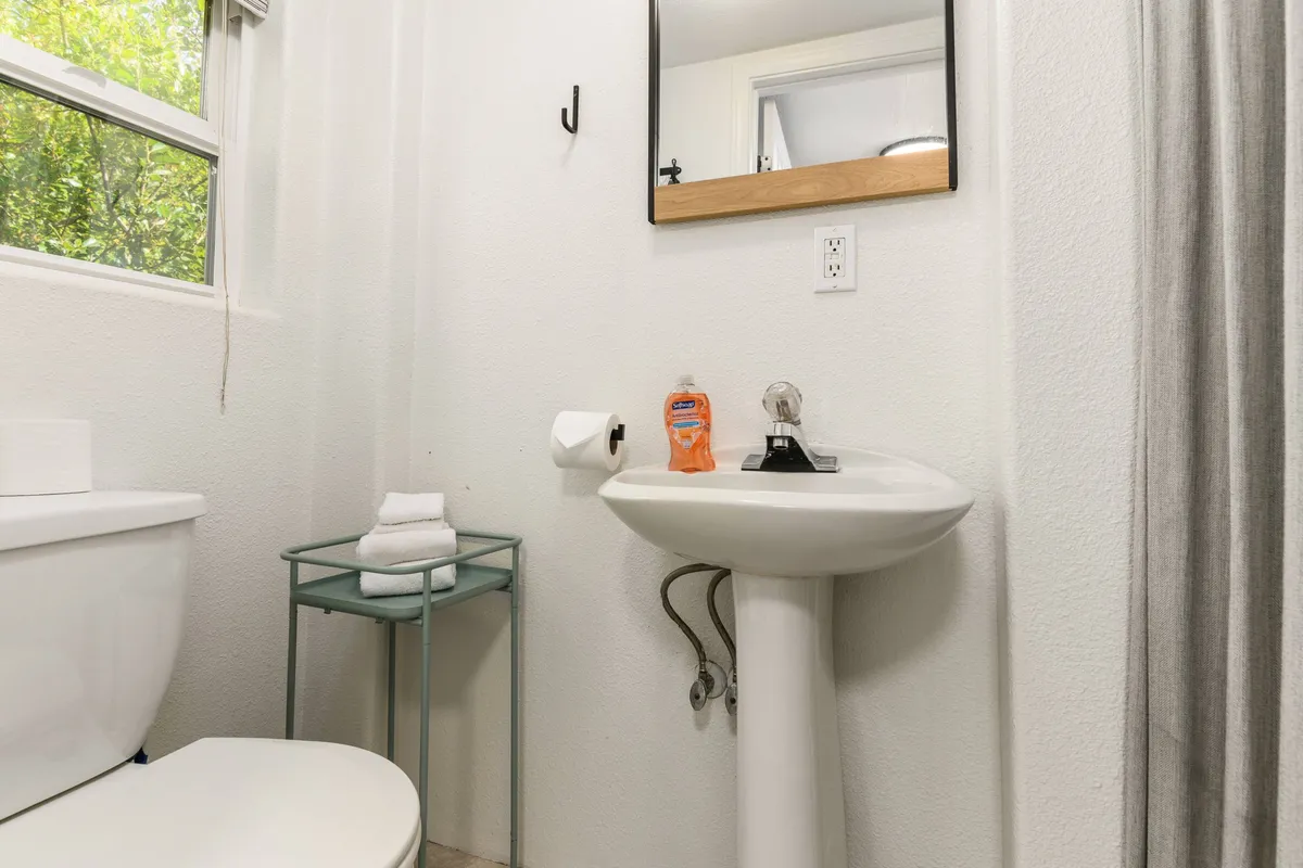 A bright, tidy bathroom with a modern sink, toilet, and mirror. Fresh towels are neatly arranged, and a pump of hand soap sits conveniently on the counter, suggesting careful attention to guest comfort.