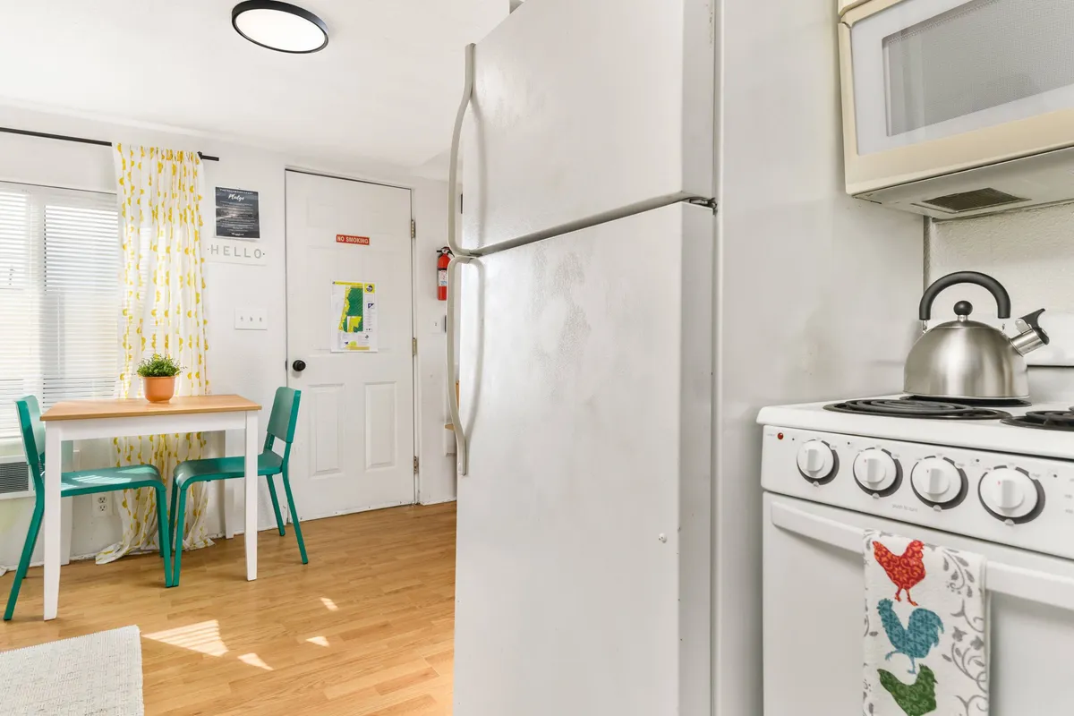 A close-up of the dining area featuring a table with chairs, refrigerator, stove, and a kettle. The setup exudes coziness and practicality, inviting guests to enjoy meals, morning coffee, or casual conversation.